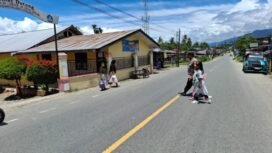 Personil kapolsek Bambel membantu anak sekolah menyeberangi di jalan Kutacane-Medan.